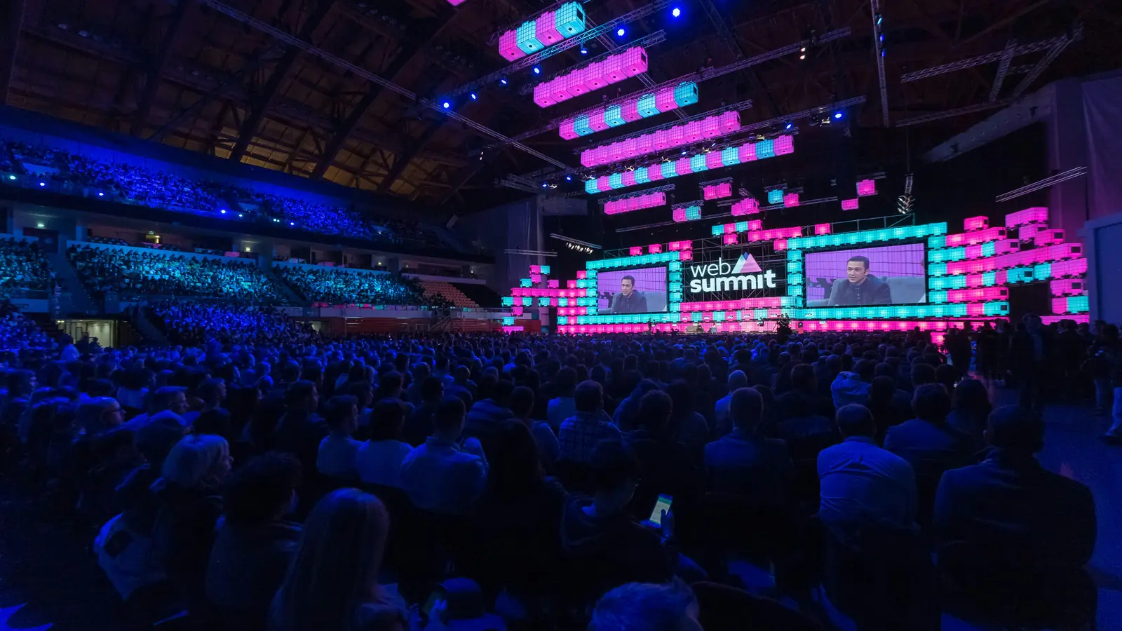 A packed arena, the stage flanked by large LED screens carrying the feed
