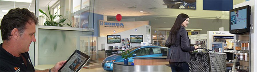 A salesperson with a tablet on a dealership floor, an information centre with product screens, and a shopper beside an in-store display