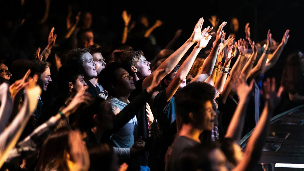 A congregation with hands raised, lit from the stage